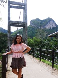 Portrait of woman standing by railing on footbridge