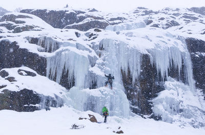 People climbing snow covered mountain during snowfall