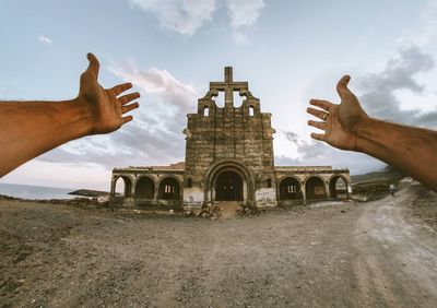 Cropped hands of man gesturing against old ruin during sunset