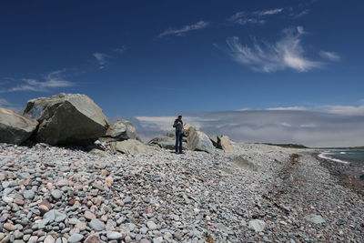 Full length of man standing by rocks at beach against sky on sunny day