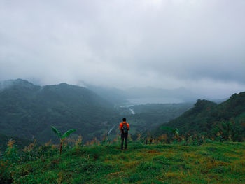 Rear view of man standing on mountain against sky