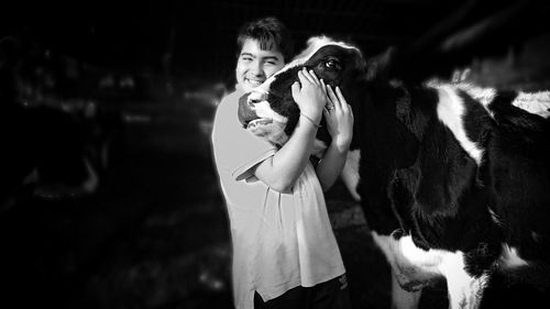 Portrait of smiling boy embracing cow at farm