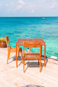 Wooden chairs on beach against sky