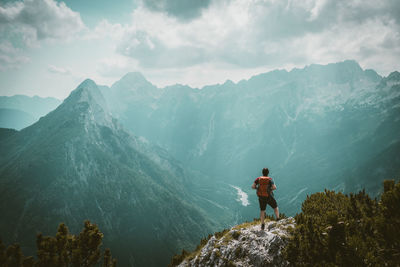 Rear view of man standing on mountain against sky