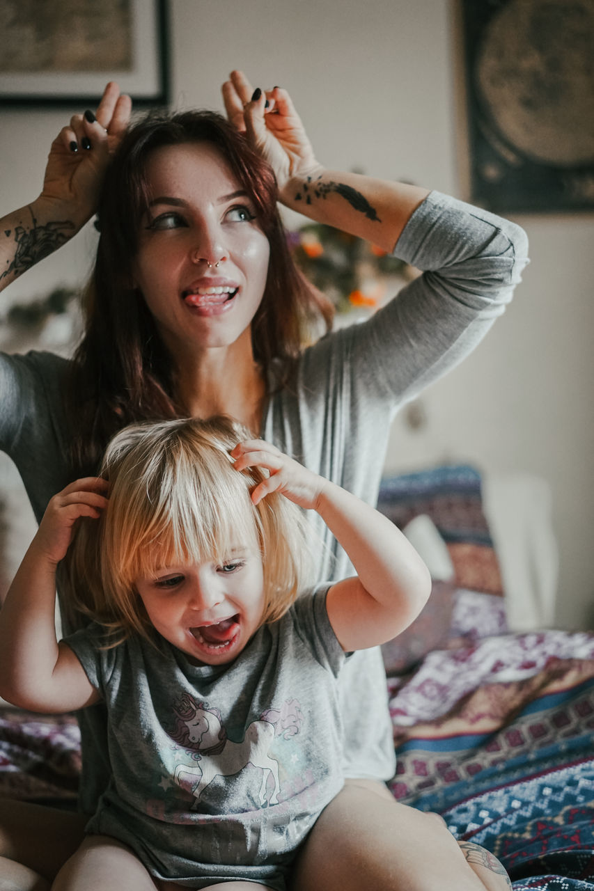 child, indoors, emotion, women, real people, portrait, focus on foreground, two people, family, young women, lifestyles, looking at camera, childhood, young adult, togetherness, casual clothing, home interior, front view, three quarter length, hair, positive emotion, beautiful woman