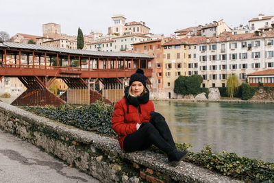 Portrait of smiling young woman sitting against buildings in city