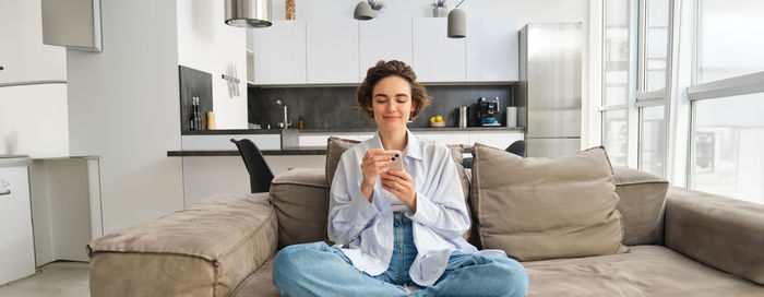 Young woman using phone while sitting on sofa at home