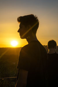 Young men standing against sky during sunset