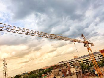 Low angle view of crane by building against sky