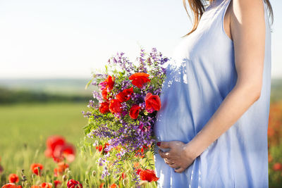 Midsection of woman holding flowering plant on field