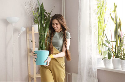 Smiling woman holding potted plant at home