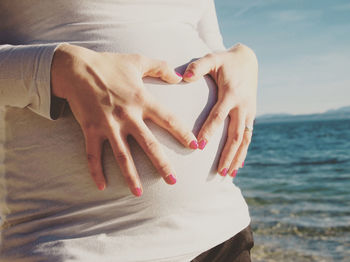 Midsection of woman touching pregnant abdomen by lake on sunny day