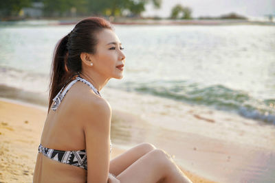 Young woman looking away while sitting on beach