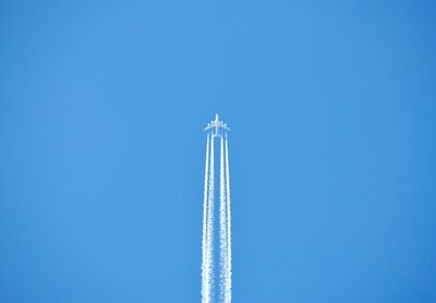 Low angle view of vapor trail emitting from airplane flying against clear blue sky