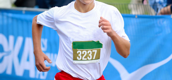 Close up of a high school cross country runner finishing a race wearing a bib on his jersey.