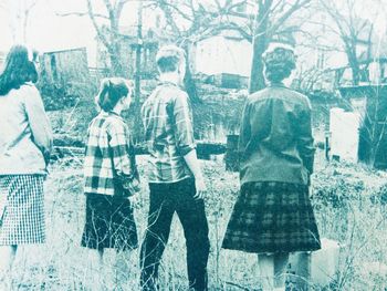 Rear view of people standing against tree in city