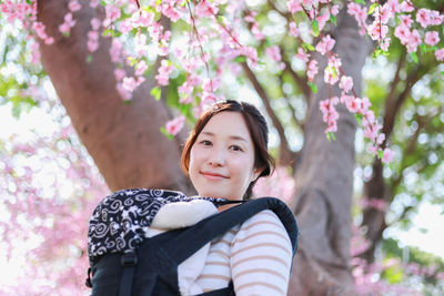 Portrait of smiling woman with pink flowers against trees