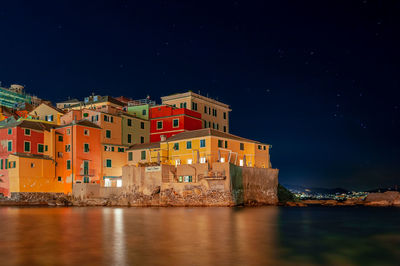 Illuminated buildings by sea against sky at night in genoa