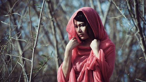 Thoughtful young woman wearing headscarf standing in forest