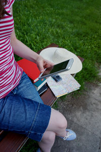 Low section of woman using mobile phone while sitting on wooden bench at park