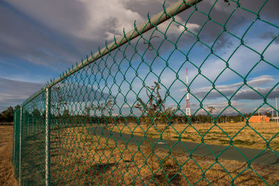 Close-up of barbed wire fence on field against sky