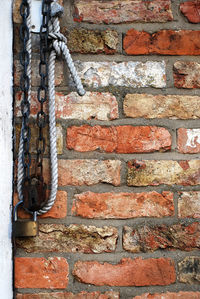 Padlocks with chain and rope hanging against brick wall