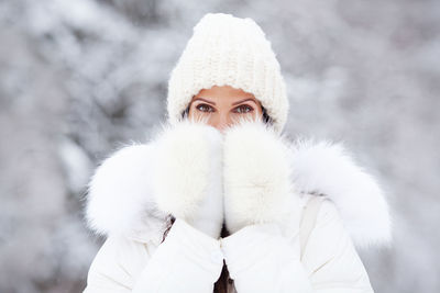 Portrait of attractive woman in white knitted hat, and fur mittens on snow cold winter nature