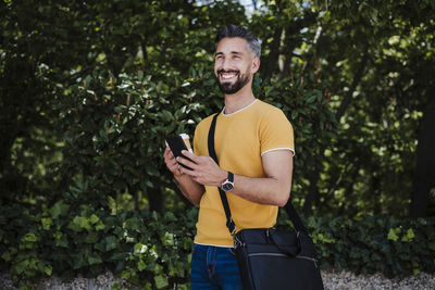 Young man using mobile phone while standing on tree