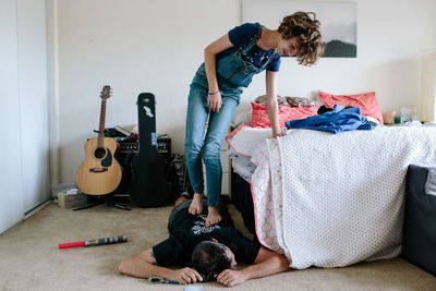 Teen girl walks on her dad's back while using bed for support