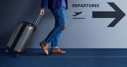 Low section of man with luggage walking at airport