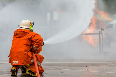 Rear view of firefighter spraying water on fire while crouching at street