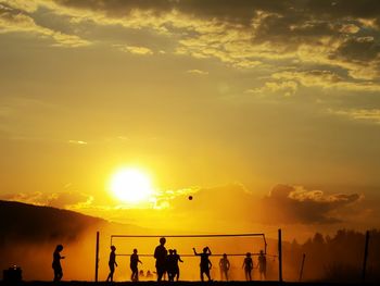 Silhouette of people playing volleyball against sky during sunset