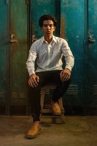 Portrait of young man sitting on table against door