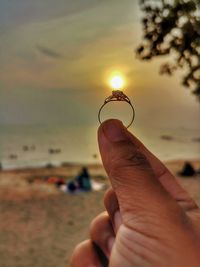 Midsection of man holding umbrella on beach against sky during sunset