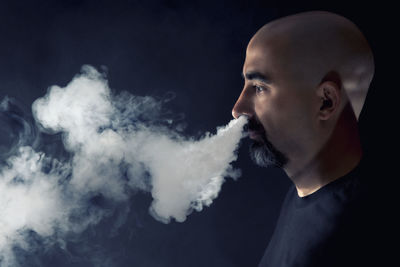 Side view of mature man smoking cigarette against black background