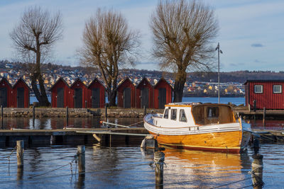 Boats moored in river by bare trees against sky