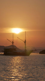 Silhouette sailboat in sea against orange sky