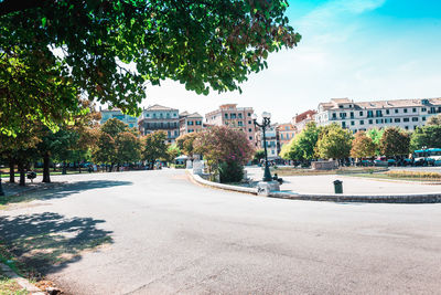 Road by trees and buildings against sky