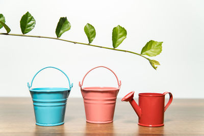 Close-up of watering can with buckets on wooden table against white background