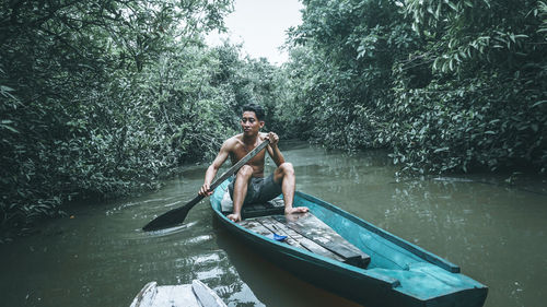 Man sitting in boat on lake against trees