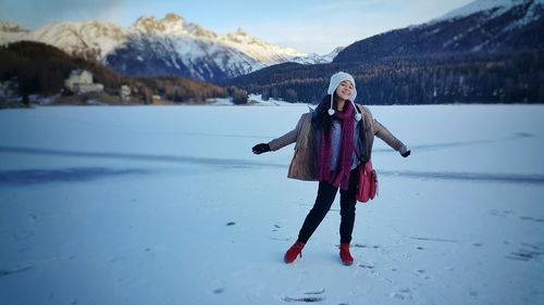 Girl with arms outstretched standing on snow covered field against mountains