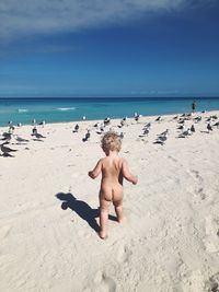 Rear view of naked baby boy walking at beach against sky