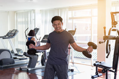 Portrait of man lifting dumbbells while making face in gym