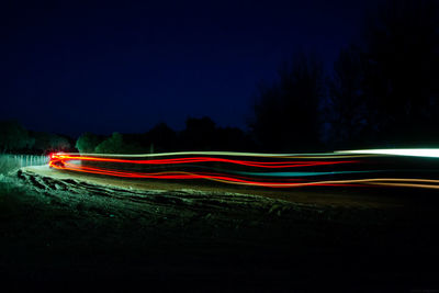 Light trails on landscape against sky at night