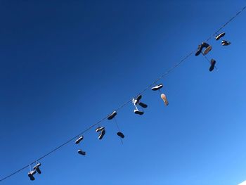 Low angle view of birds on cable against clear blue sky