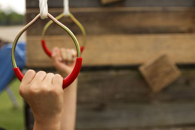 Cropped hands hanging on rings at park