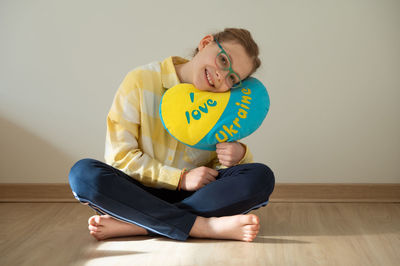 Portrait of smiling young woman holding heart shape against wall