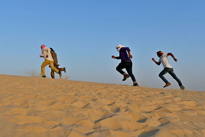 People running on sand at beach against clear sky