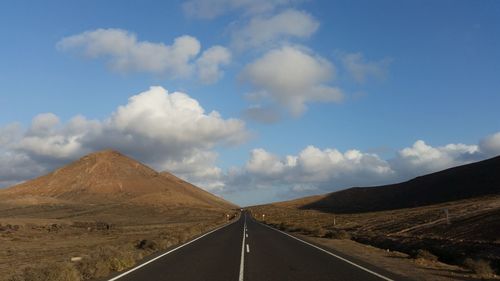 Road leading towards mountains against sky