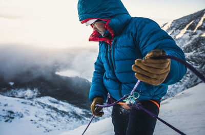 Male climber belays his lead climber during a cold winter alpine climb